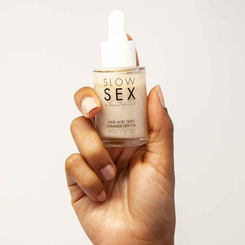 Front View of Bijoux Indiscrets Slow Sex Shimmer Dry Oil Bottle being held by hand on a white background