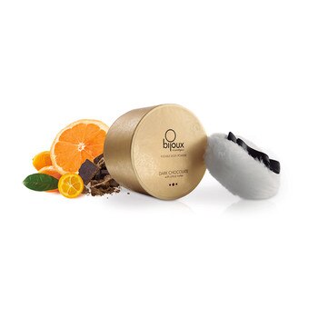 An image of the bijoux kissable body powder round gold container with application puff. Next to it are oranges and chocolate, to indicate the dark chocolate and citrus flavor.