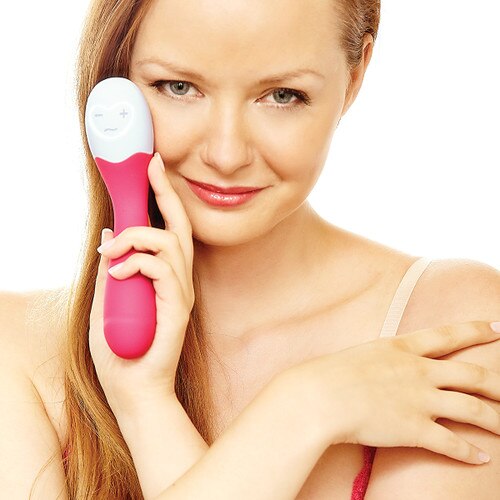 An image of a blond woman smiling coyly at the camera while holding a pink Lovelife Cuddle in her hand by her face.