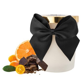 An image of the bijoux Melt By Heart dark chocolate scented massage candle. It is in a jar with a black ribbon. Next to it are oranges and chocolate, to indicate the dark chocolate and citrus flavor.