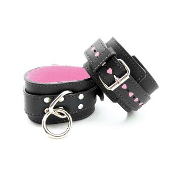 An image of black leather buckled wrist cuffs with soft pink interior and rows of little pink hearts along the straps.