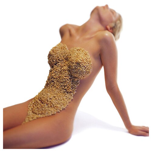 Erotic photography from The New Intercourses. A naked woman sits with her back arched, her front covered in nuts and seeds.